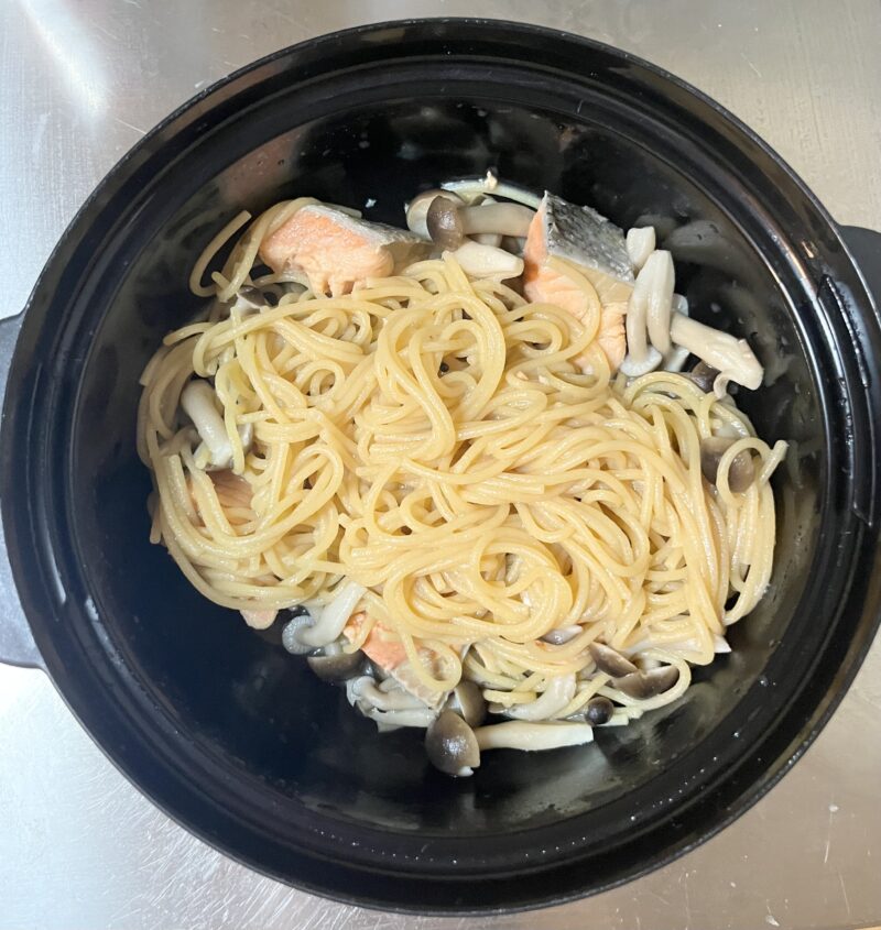 レンジ加熱後、パスタと鮭、きのこの旨みが詰まった容器から余分な水を捨てた後の手順写真。