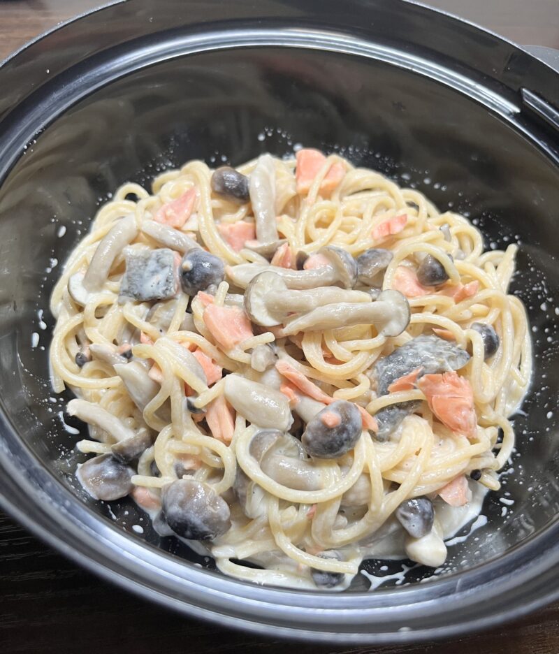 濃厚なクリームソースが全体に絡んだ、鮭ときのこのクリームパスタの盛り付け写真。鮭をくずして細かくしている様子。