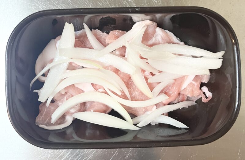 耐熱容器に薄切り玉ねぎと豚こま肉を入れて、電子レンジで2分加熱する前の工程。