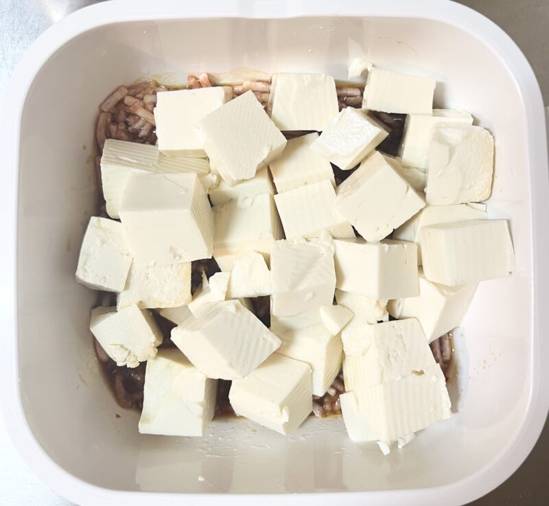 調味料とひき肉の上に木綿豆腐をのせてレンジで加熱する前の様子