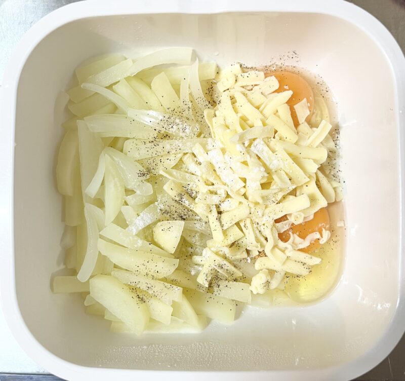 耐熱容器の中で、じゃがいも・玉ねぎと卵、コンソメ、チーズを混ぜ合わせる前の工程。