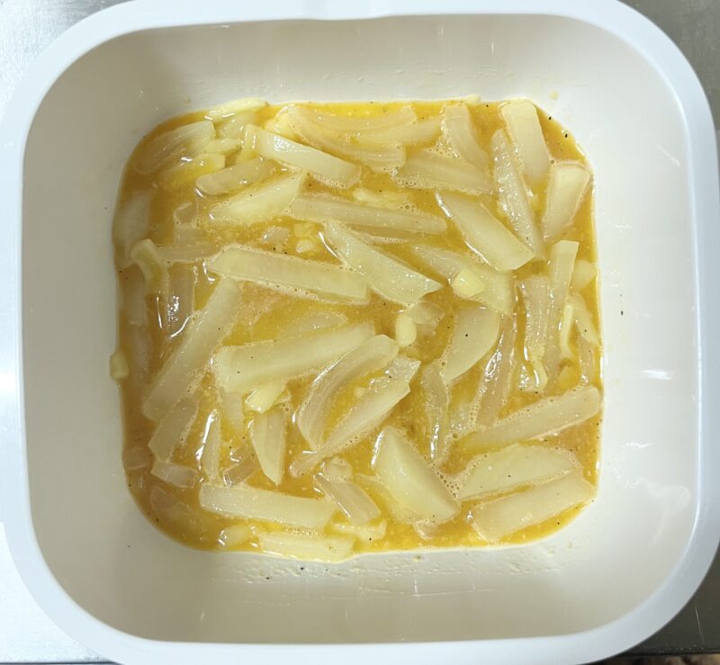 耐熱容器の中で、じゃがいも・玉ねぎと卵、コンソメ、チーズを混ぜ合わせた後の工程。