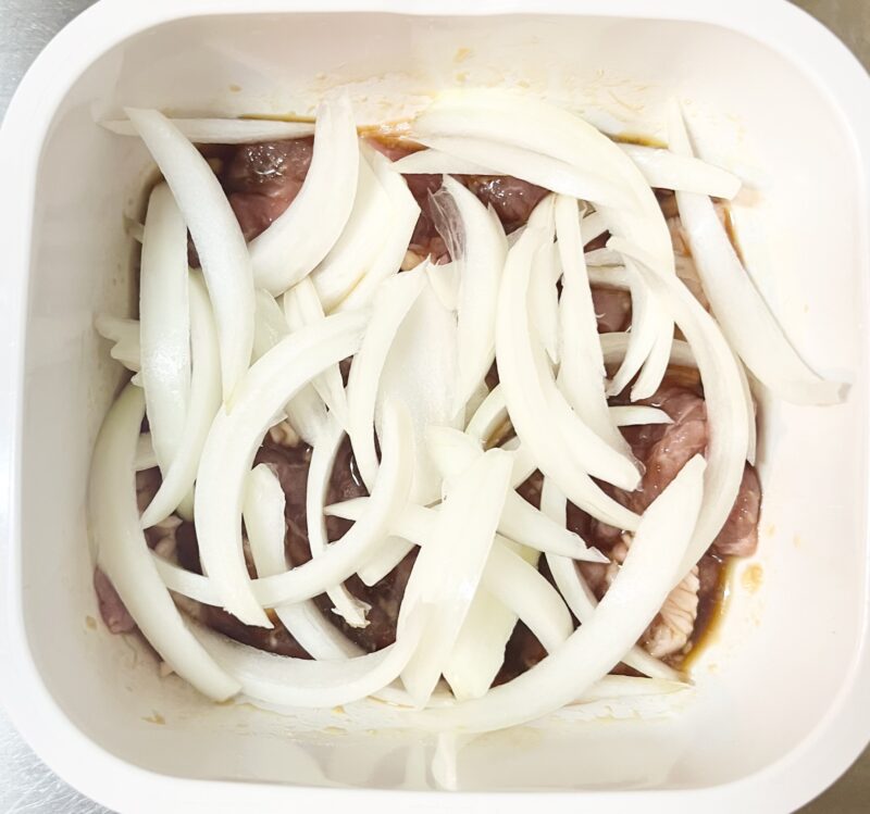 味付けした豚こま肉の上に薄切りにした玉ねぎをのせたレンジ加熱前の状態