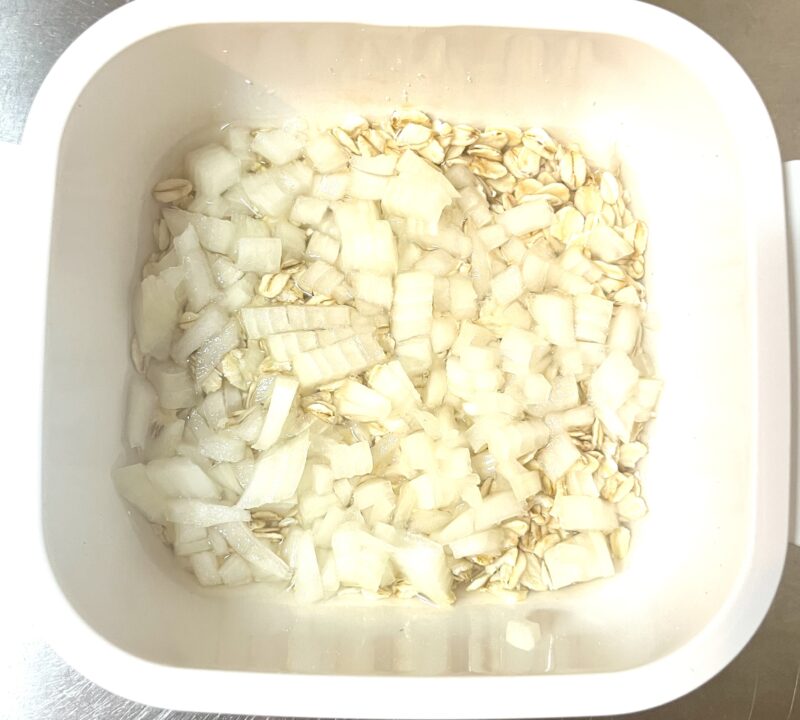 みじん切りにした玉ねぎと米化するため、耐熱容器入れたオートミールとひたひたになるくらいの水の加熱前の様子