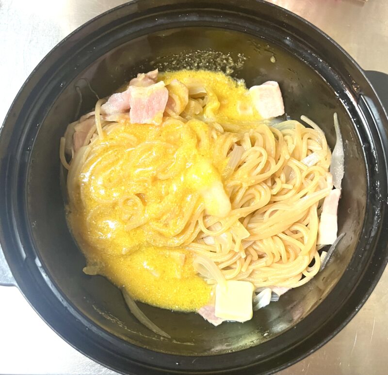 茹で上がった熱々のパスタに、バターとにんにくチューブと卵液を加えて余熱で溶かし、麺に絡めている仕上げの工程。