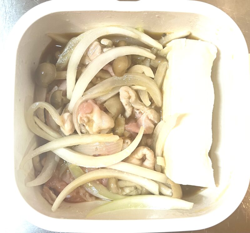 豚肉、玉ねぎ、しめじ、木綿豆腐が入った容器に調味料を入れた様子