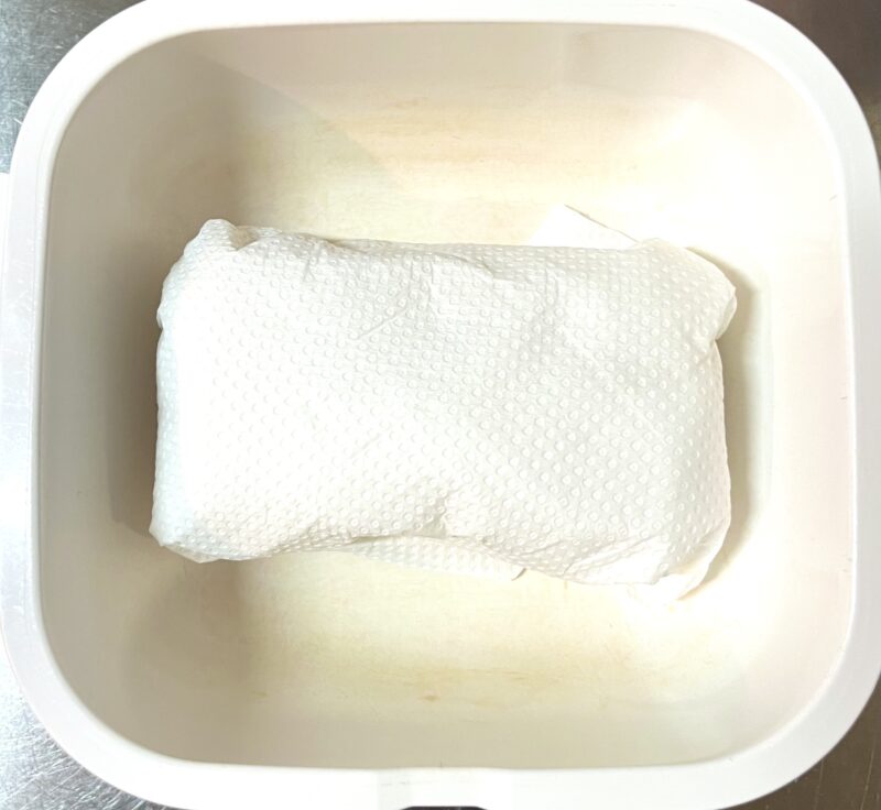 水切りのため、木綿豆腐をキッチンペーパーでつつみ、耐熱容器に入れたレンジで加熱前の様子