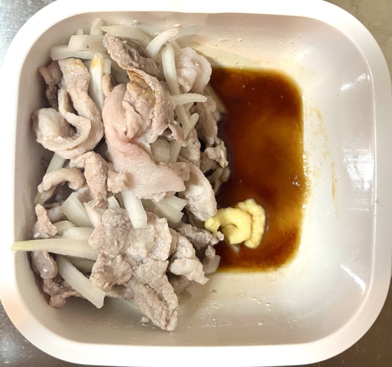 電子レンジで加熱され色が白く変わった豚肉と玉ねぎに調味料を加える様子