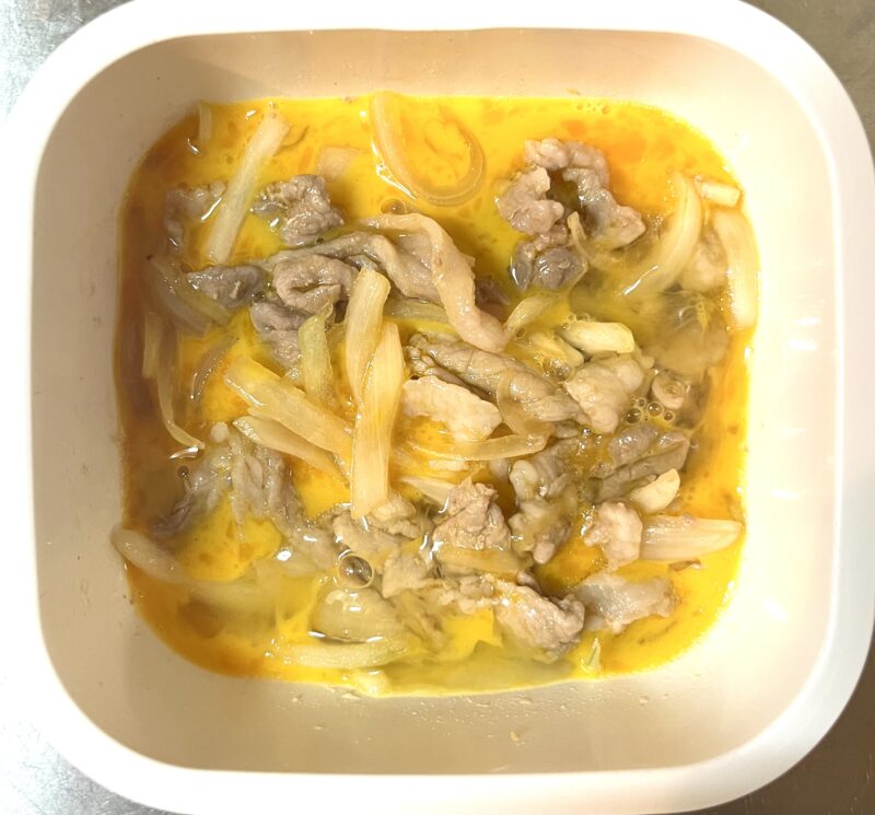 タレを絡めた加熱済みの豚肉と玉ねぎの上に溶き卵が全体に回しかけられている様子