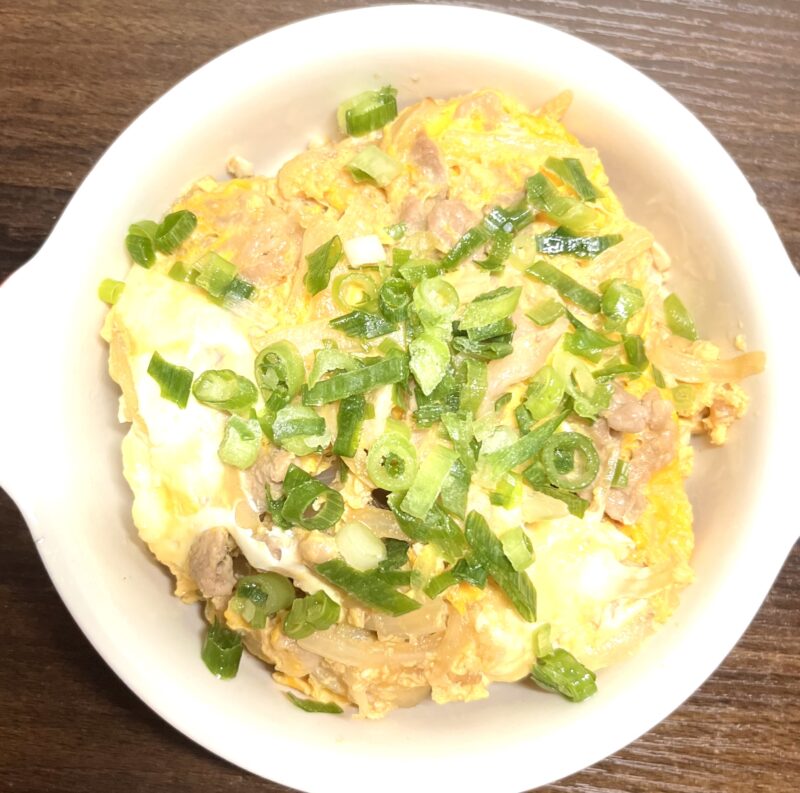 完成した豚たま他人丼の表面に、仕上げとしてたっぷりの緑鮮やかなきざみねぎが散らされている様子